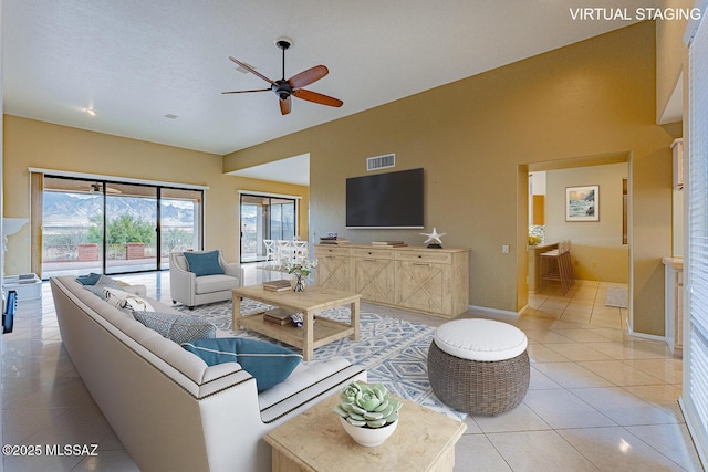 living area with light tile patterned floors, a ceiling fan, visible vents, vaulted ceiling, and baseboards