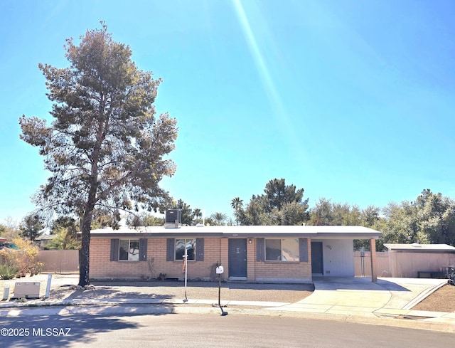 ranch-style home featuring fence, an attached carport, concrete driveway, and brick siding