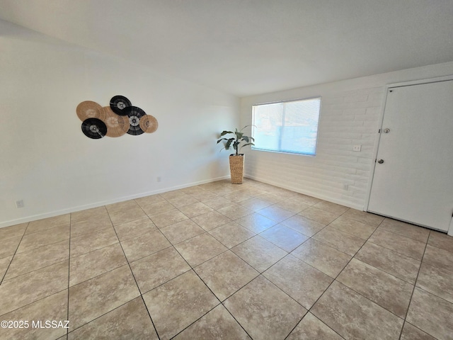 tiled empty room featuring brick wall and baseboards