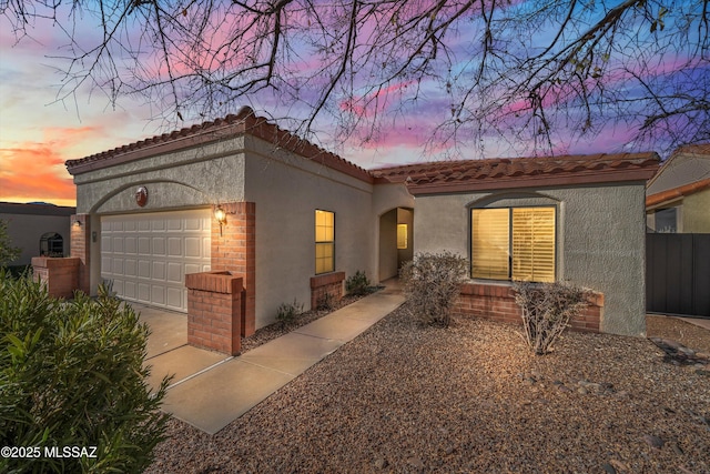 mediterranean / spanish house with a tiled roof, an attached garage, and stucco siding