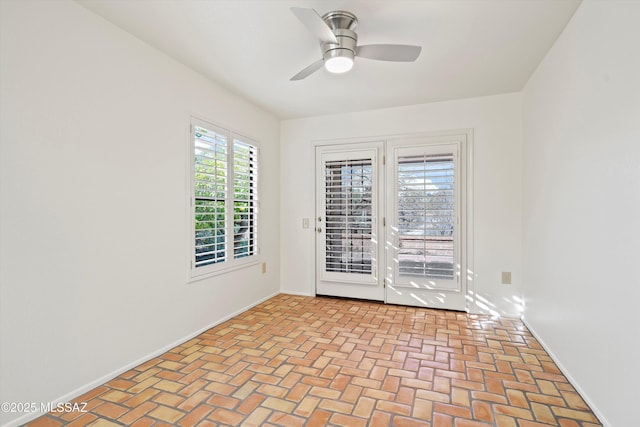 spare room with brick floor, baseboards, and a ceiling fan