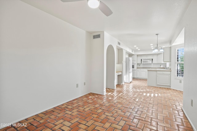 unfurnished living room with brick floor, arched walkways, visible vents, a sink, and ceiling fan with notable chandelier