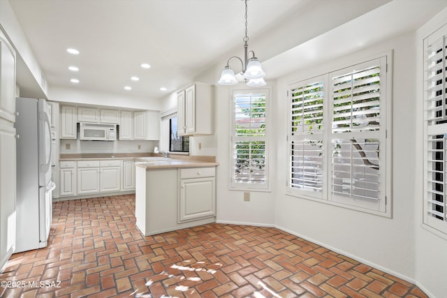 kitchen with brick floor, light countertops, hanging light fixtures, white cabinets, and white appliances