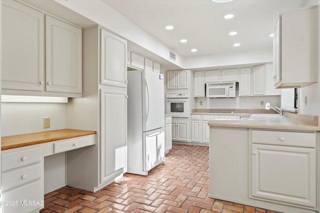 kitchen with recessed lighting, white appliances, white cabinetry, light countertops, and built in desk