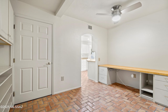 unfurnished office with ceiling fan, brick floor, built in study area, and visible vents