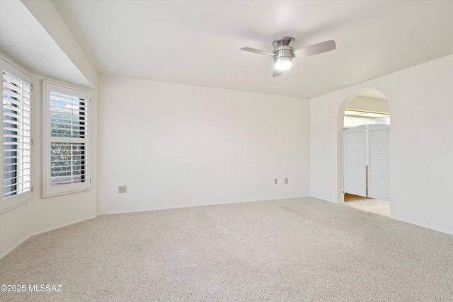 empty room with arched walkways, ceiling fan, and light carpet