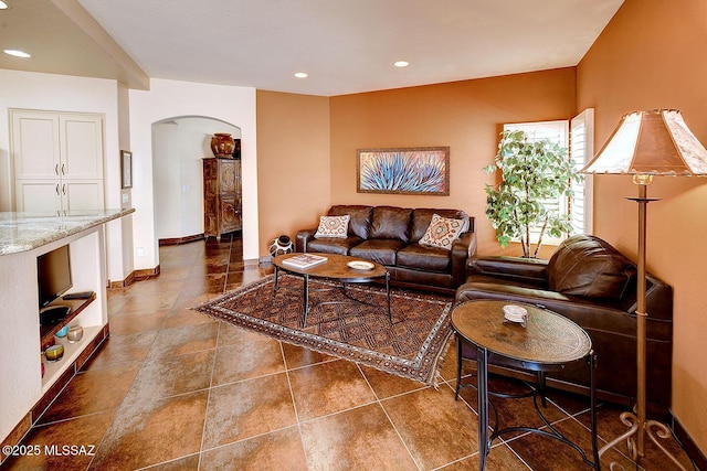 living room featuring baseboards, arched walkways, dark tile patterned flooring, and recessed lighting