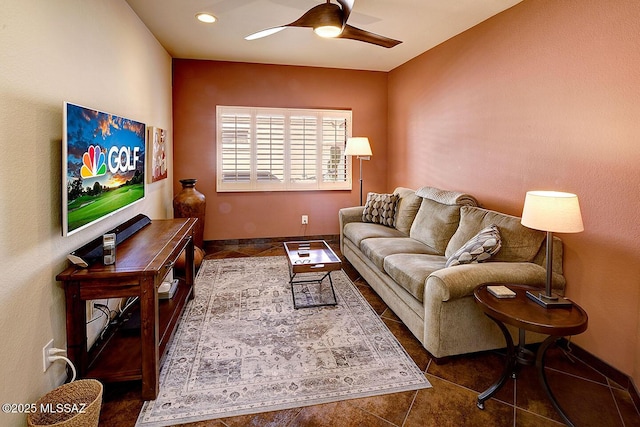 living area featuring ceiling fan, dark tile patterned flooring, and baseboards