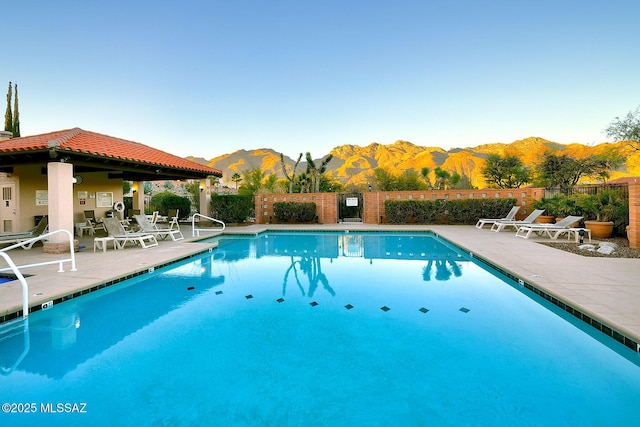 community pool with a mountain view, a patio, and fence