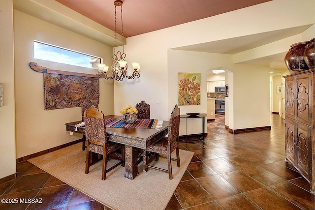 dining area featuring arched walkways, dark tile patterned floors, an inviting chandelier, and baseboards