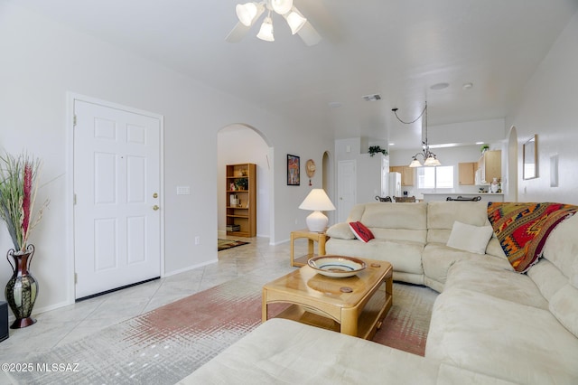 living area featuring arched walkways, visible vents, light tile patterned flooring, ceiling fan, and baseboards