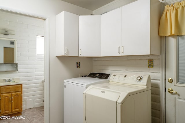 washroom featuring washer and dryer, cabinet space, brick wall, and light tile patterned floors