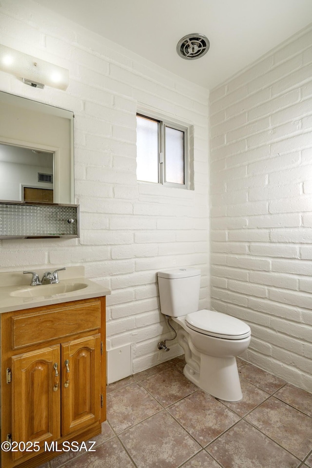bathroom with visible vents, toilet, tile patterned floors, vanity, and brick wall
