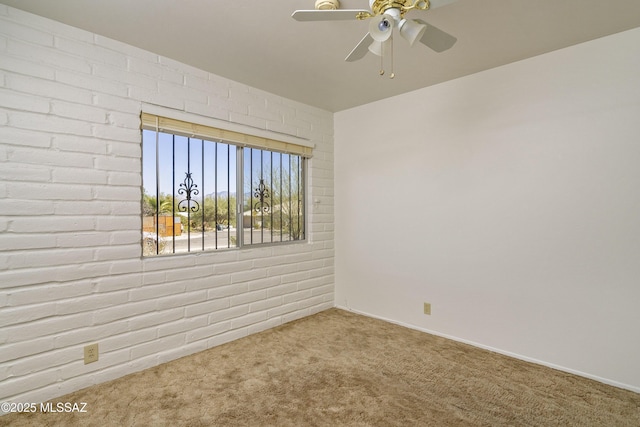 empty room with brick wall, carpet flooring, and a ceiling fan
