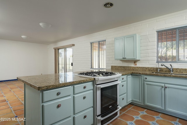 kitchen with white range with gas stovetop, a sink, a healthy amount of sunlight, and a peninsula
