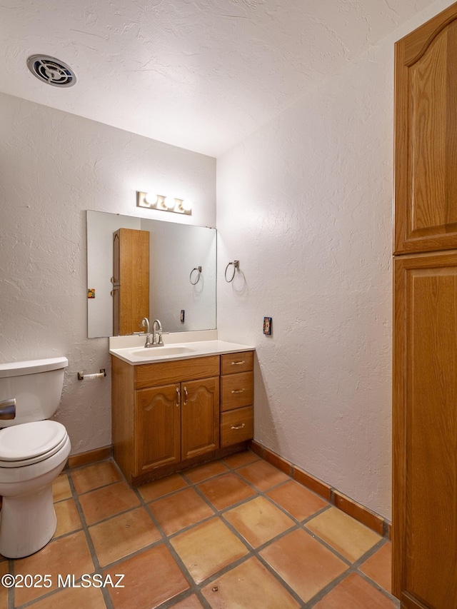 bathroom featuring visible vents, toilet, vanity, and a textured wall