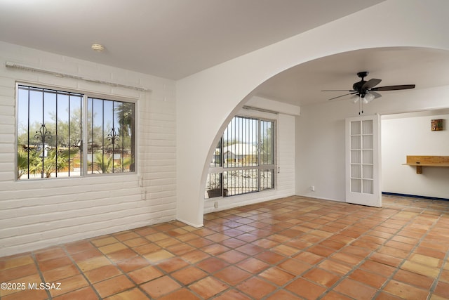 spare room with a ceiling fan, arched walkways, tile patterned flooring, and brick wall