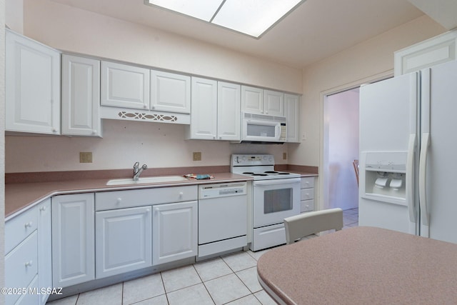 kitchen with light tile patterned floors, white appliances, a sink, and white cabinets