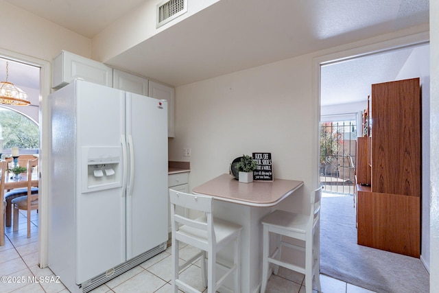 kitchen featuring white refrigerator with ice dispenser, visible vents, light countertops, white cabinetry, and a notable chandelier