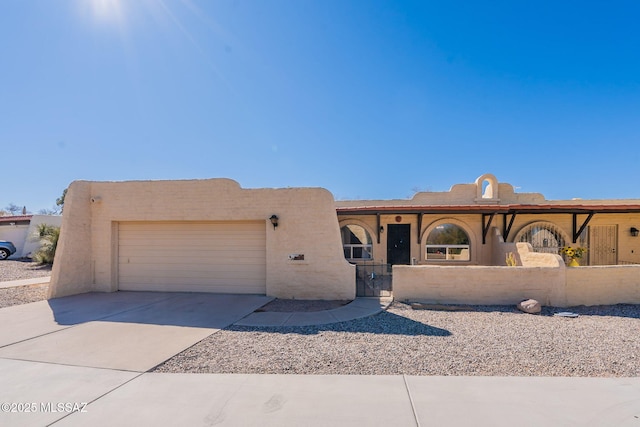 pueblo-style house featuring concrete driveway, a fenced front yard, an attached garage, and stucco siding