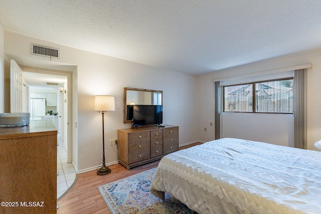 bedroom featuring light wood-style floors, visible vents, a textured ceiling, and baseboards