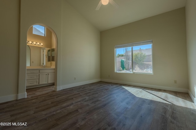 unfurnished bedroom featuring dark wood-style floors, high vaulted ceiling, ensuite bathroom, and baseboards