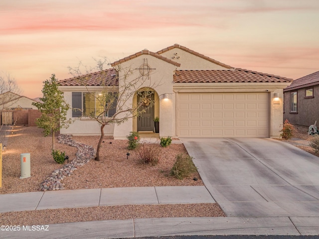 mediterranean / spanish-style house with driveway, an attached garage, a tiled roof, and stucco siding