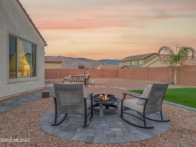 patio terrace at dusk with a fenced backyard, a mountain view, and a fire pit