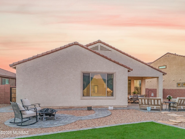 back of property at dusk featuring an outdoor fire pit, a patio area, fence, and stucco siding