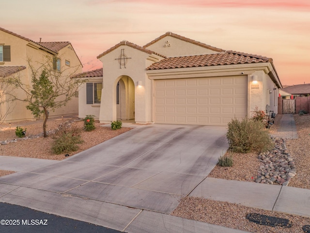 mediterranean / spanish house featuring a garage, fence, a tile roof, concrete driveway, and stucco siding