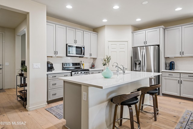 kitchen with appliances with stainless steel finishes, a kitchen bar, light wood-style flooring, and recessed lighting