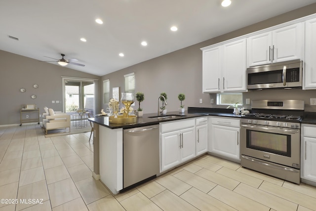 kitchen with stainless steel appliances, a peninsula, a sink, white cabinetry, and dark countertops