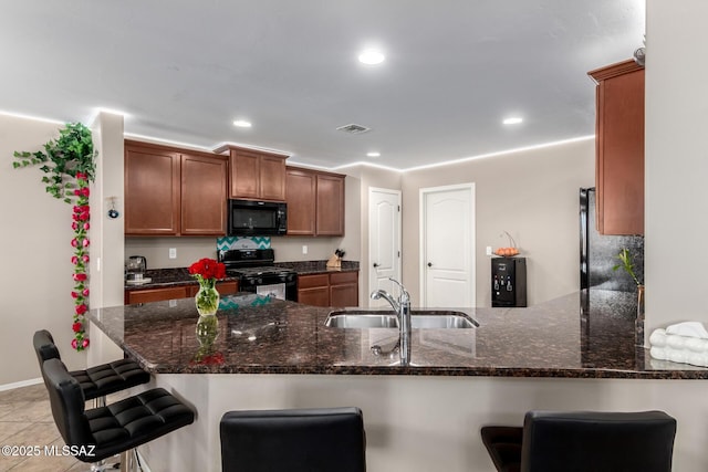 kitchen featuring dark stone counters, a sink, a peninsula, and black appliances