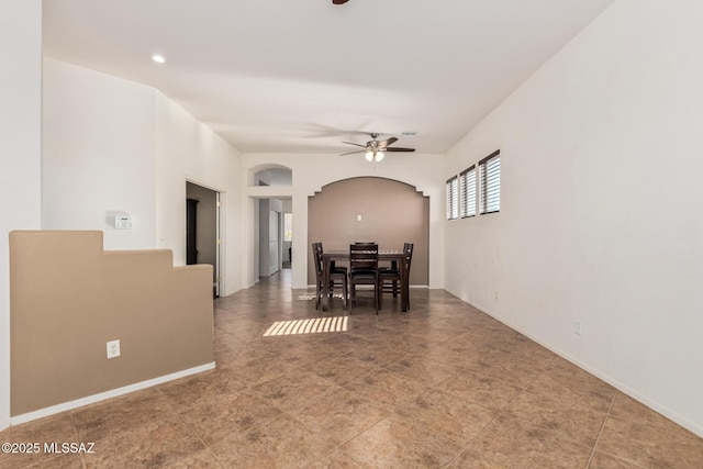 dining space featuring arched walkways, a ceiling fan, and baseboards