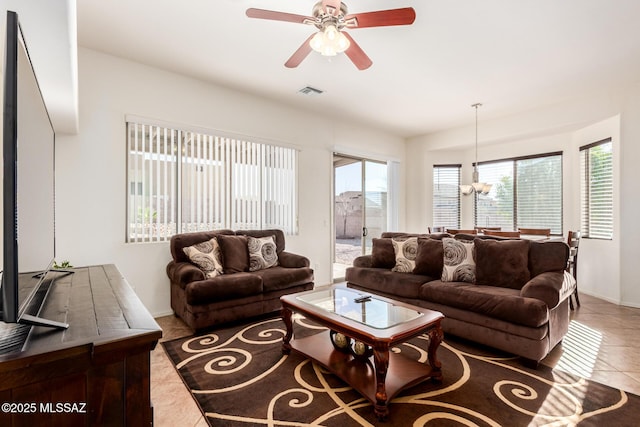 tiled living area with baseboards, visible vents, and ceiling fan with notable chandelier