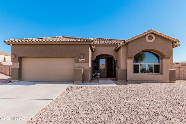 mediterranean / spanish house with an attached garage, a tile roof, concrete driveway, and stucco siding