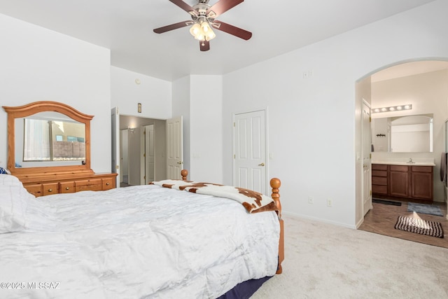 bedroom with arched walkways, light carpet, a sink, ensuite bath, and baseboards