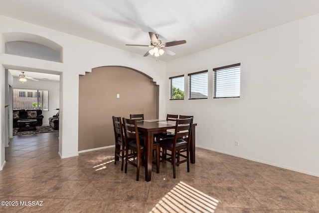 dining room with arched walkways, ceiling fan, dark tile patterned flooring, and baseboards