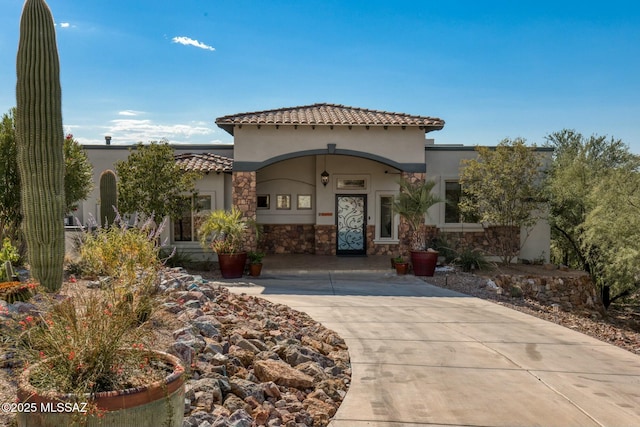 mediterranean / spanish-style house featuring stone siding, a tiled roof, and stucco siding