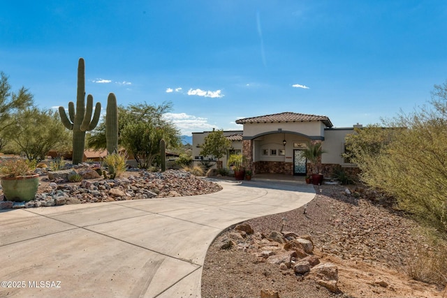 view of front facade with stone siding, a tile roof, concrete driveway, and stucco siding