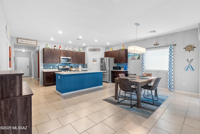 kitchen featuring decorative light fixtures, light countertops, appliances with stainless steel finishes, backsplash, and a center island with sink