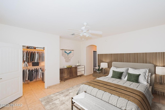 bedroom with arched walkways, light tile patterned floors, a spacious closet, and a ceiling fan