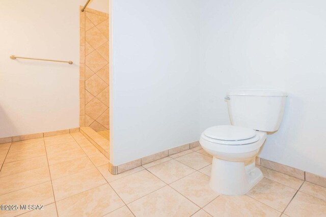 full bath featuring tile patterned floors, toilet, tiled shower, and baseboards