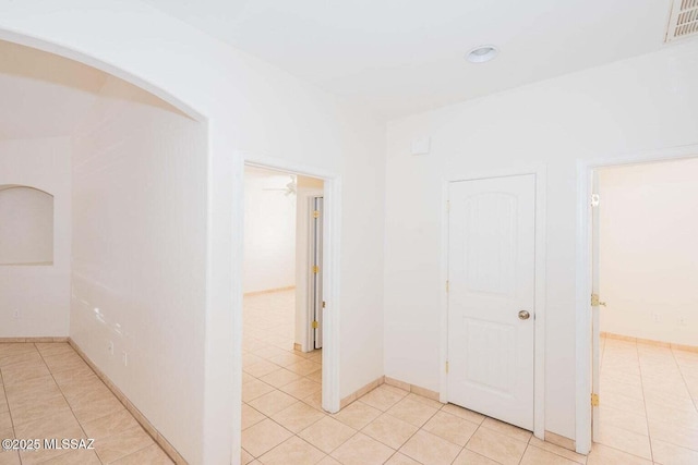 hallway featuring light tile patterned floors, visible vents, arched walkways, and baseboards