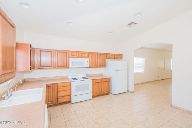 kitchen featuring white appliances, visible vents, arched walkways, light countertops, and a sink