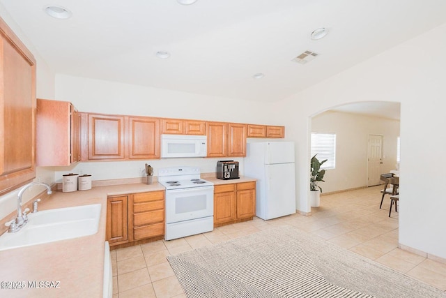 kitchen featuring white appliances, light tile patterned floors, arched walkways, a sink, and light countertops