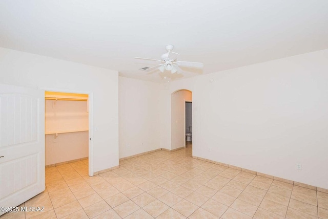 unfurnished room featuring arched walkways, ceiling fan, and light tile patterned floors