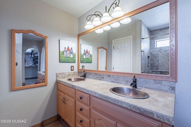bathroom featuring double vanity, backsplash, tiled shower, and a sink