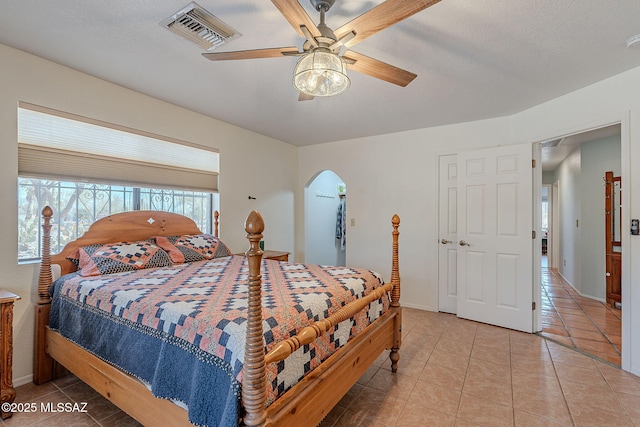 bedroom featuring light tile patterned floors, baseboards, visible vents, arched walkways, and ceiling fan
