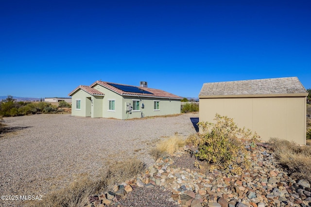 back of house with a chimney, stucco siding, a tile roof, and roof mounted solar panels